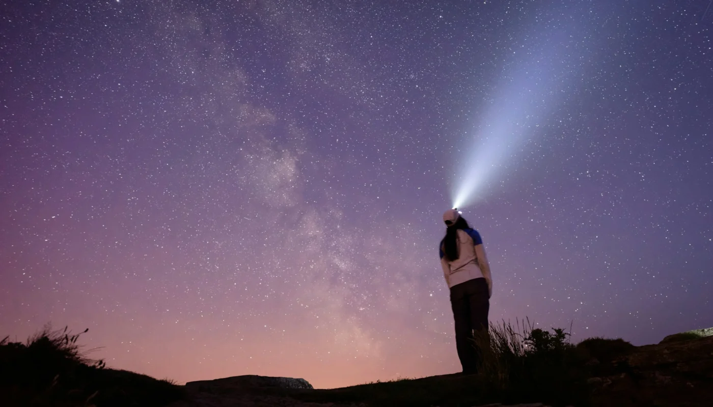 randonneur avec lampe frontale illuminant le ciel étoilé la nuit
