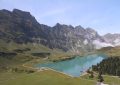 Turquoise lake surrounded by green hills and mountains.
