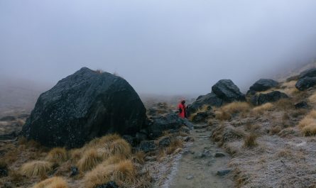 randonneur en rouge sur sentier GR entre rochers et herbes jaunes sous brouillard